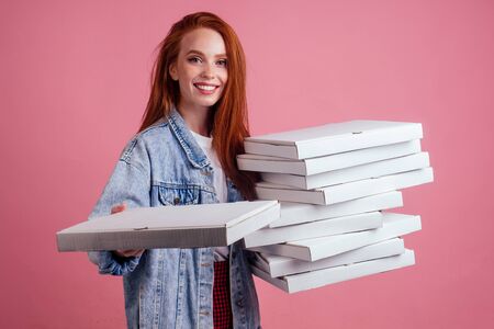pretty long ginger red-haired woman holding a lot of boxes with fast food snack isolated pink...