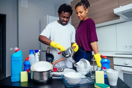 Young happy african american couple is washing dishes while doing cleaning at home