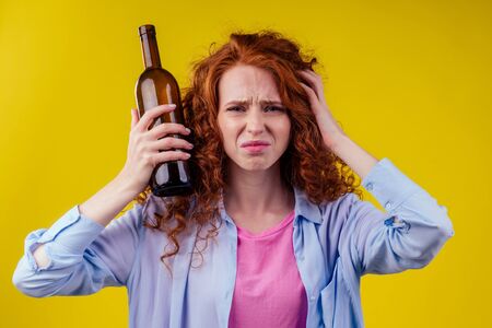 curly redhead ginger woman drinking beer and feeling bad mood in csudio yellow backgroundの写真素材
