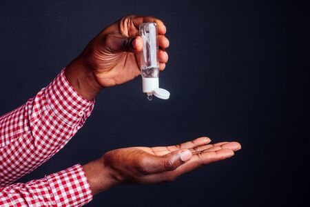 close up hands of afro male useing antiseptic in studio black background.washing hands after going to the toilet conceptの写真素材