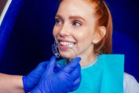beautiful redhead ginger woman with open mouth and mouthpiece at the dentist wearing plastic...