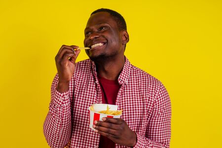 handsome latin man eating fries with appetite and enjoyment in studio yellow backgroundの写真素材
