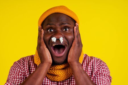 young african american male wearing red checkered shirt with knitted scarf and hat feeling bad unwell with fever heat and chills in studio yellow background.flu and virus conceptの写真素材