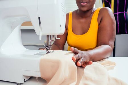 Young african american dressmaker woman sews clothes on sewing machine at tailor office it tropical summer style .の写真素材