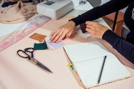 beautiful seamstress with long hair writes in a notebook. the tailor creates a collection of outfits. young woman designer clothes working with leather.の写真素材