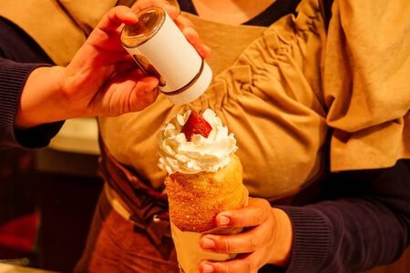 woman with an appetite eats a traditional Czech sweet Trdelnik with vanilla cream and strawberries...