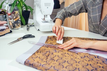 Portrait of a seamstress in in a checkered jacket working in her sewing studio,she showing inside of...