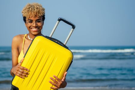 mixed race brazilian hispanic woman wearing yellow swimming suit bra and holding travel suitcase on...