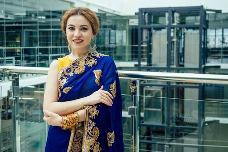 Young elegant indian business woman in a stylish blue sari arms crossed in a modern office with...