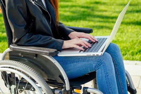 redhead ginger freelancer woman sitting in wheelchair and working by laptop in summer park,の写真素材
