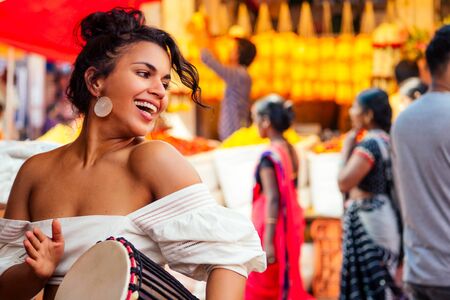indian wearing fashionable clothes posing in asian bazar playing djembe music drummer