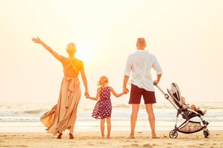 happy parents and two little girls children looking at sunset on the beach and waving .の写真素材