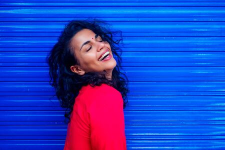 Attractive beautiful happy young latin hispanic woman with teak bindi on forehead smiling on blue wall street backgroundの写真素材
