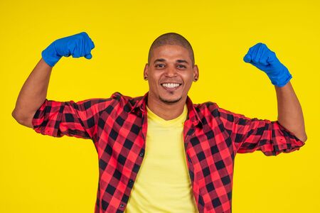 latin brazilian cleaning man wearing ribon gloves in studio yellow background