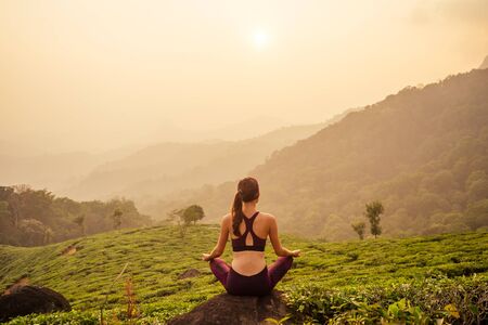 woman in violet cloth doing yoga on tea plantations in Munnar hill Kerala India.