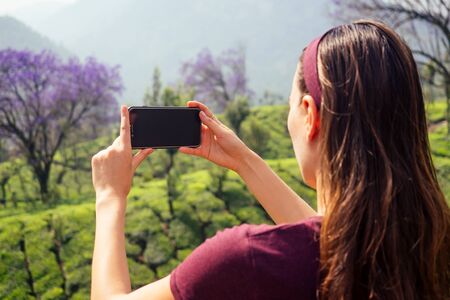young girl enjoying a good morning taking picture photo on camera of phone in tea plantations in India Munnar Keralaの写真素材