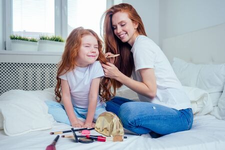 cute foxy hair little girl applying make up and doing hairstyle to redhaired ginger mother at bedroom beautican girlish spa day.の写真素材