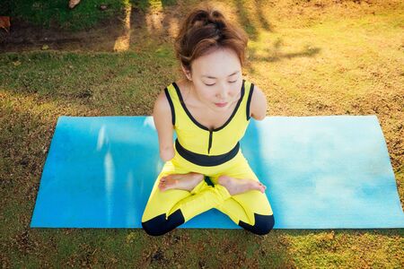 happy asian armless woman warming up before swimming at the tropical beach on yoga matの写真素材