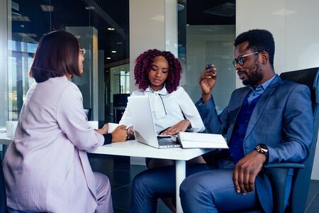 creative team of multiracial men sitting round the desk in formal clothes talking over new project in meeting roomの写真素材