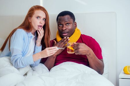 african american man in knitted scarf and redhaired ginger woman in pajamas lying in bed day off...