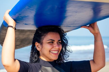 indian woman in diving suit spenting time at Goa sea.she carrying surfboard on head