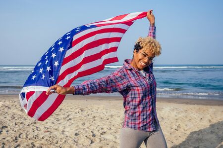 happy afro american woman holding usa flag at sunny tropical beach.4th of July Independence Day...