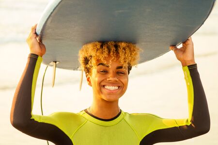 african american girl with surf board on beach going to the water