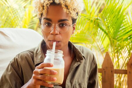 beautiful brazilian smiling girl drinking cold icy coffee or smoothie in cafe from a glass jarの写真素材