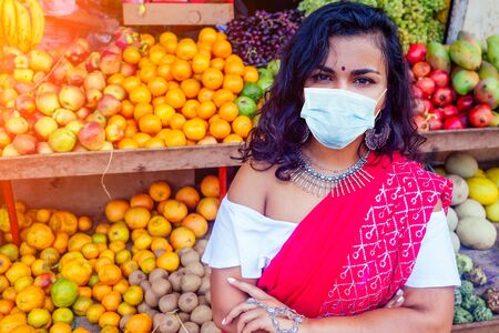 Portrait of beautiful traditional Indian seller business woman in red sari dress with customer in street Delhi market india mumbai.Happy girl shopper in a supermarket fruits vegetable shop Kerala Goa.の写真素材