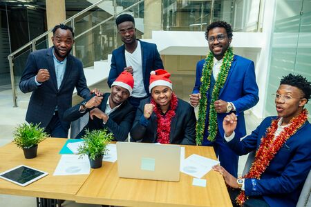 happy group of indian and african american people drinking toast from cup,wearing santa hat and tinselの写真素材