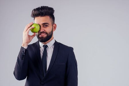 young handsome black hair man in stylish business suit eating green apple in studio isolate white backgroundの写真素材