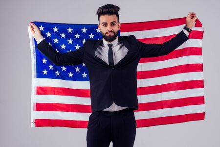 arabian young handsome black hair man in stylish business suit holding american flag in studio isolate white background.Independence Day conceptの写真素材