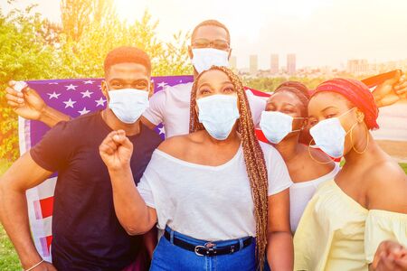 Group of girls and boys in medical mask smiling with American flag in spring park autumn evening...