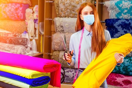 redhaired ginger dressmaker woman cropping cutting textile in shop behind her background stock with bright sequins sparkling fabricの写真素材
