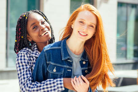 cheerful afro and european lesbian women laughing and looking at camera at summer downtown cityの写真素材
