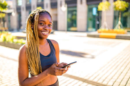 african american girl with long yellow dreadlocks pigtails useing trainer work out app outdoors in...