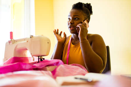 african american woman tailor creates a collection of outfits talking with client by phoneの写真素材