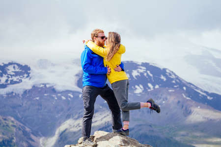Couple of young hikers in yellow and blue raincoats standing on mountains in Elbrus