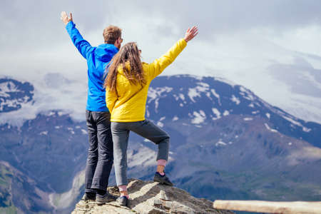 Couple of young hikers in yellow and blue raincoats standing on mountains in Elbrusの写真素材