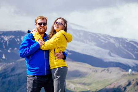 Couple of young hikers in yellow and blue raincoats standing on mountains in Elbrus