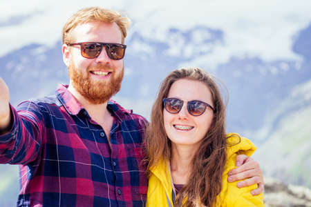 Couple of young hikers in yellow and blue raincoats standing on mountains in Elbrus