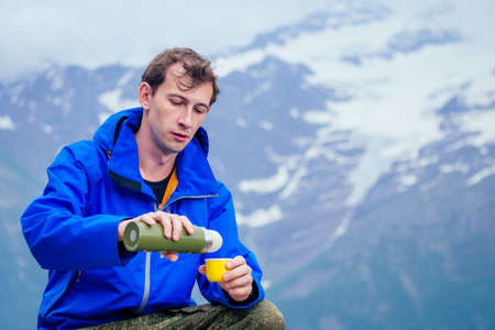 man in blue jacket with rain in mountains tea drinking