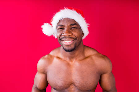 naked nude african american man holding gift box with white ribbon tie bow in red studio backgroundの写真素材