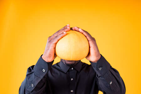 People and Halloween preparation concept, man holding small pumpkin in studio yellow backgroundの写真素材