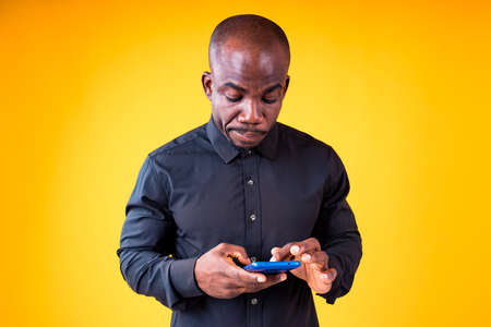 young man holding phone looking at smartphone isolated on yellow studio background
