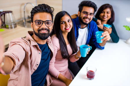 four indian friends sitting at kitchen and making online video chat