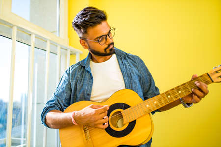 Cheerful handsome young man playing guitar and smiling in new cozy apartmentの写真素材