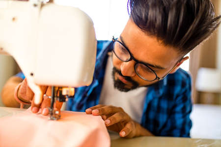arabian man designer sewing clothes on sewing machine in studio workplace homeの写真素材