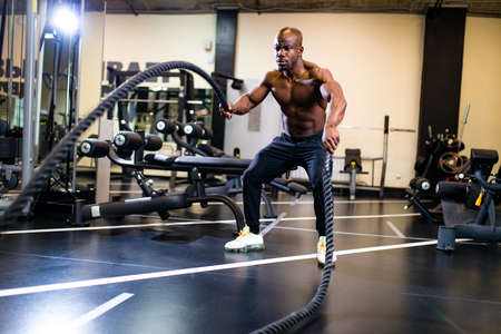 young african muscular athlete working out with ropes in gym