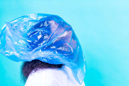 unhappy female with plastic bag on her head against blue wall studioの写真素材